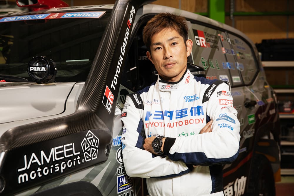 Miura Akira stands with his arms crossed in front of the Land Cruiser.