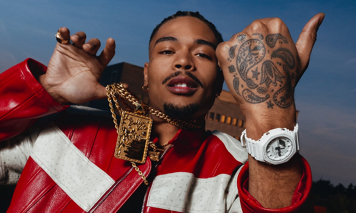 Artie 5ive mostra un orologio G-SHOCK GA-2100-7A7 bianco al polso tatuato, mentre indossa collane d’oro e una giacca di pelle rossa e bianca.