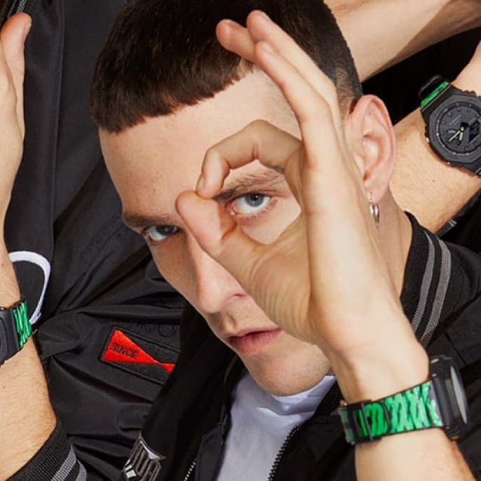 Un uomo guarda attraverso la mano verso la macchina fotografica e indossa l'orologio G-SHOCK nero e verde al polso 