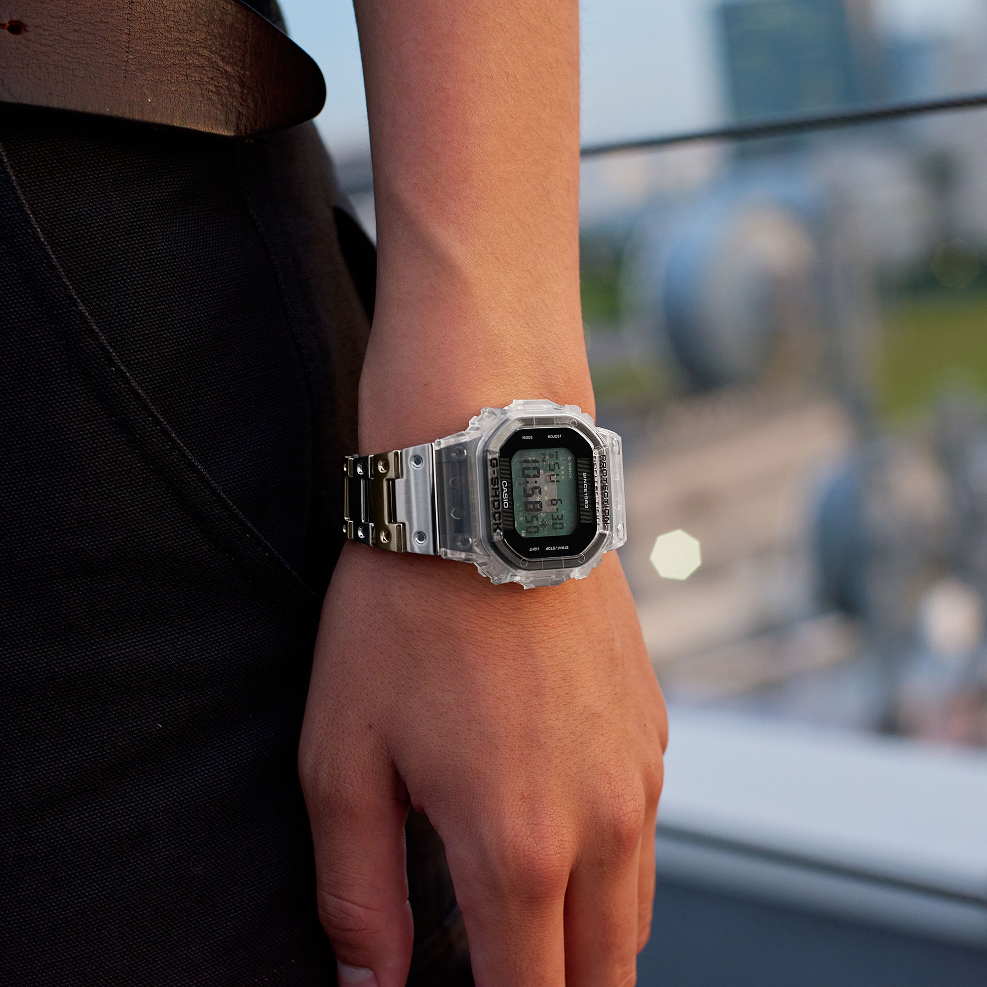 L'orologio digitale rettangolare “DWE-5640RX-7” con cassa trasparente e cinturino oro-argento al polso di un uomo.