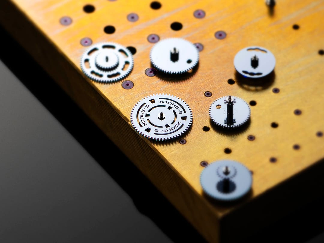 Singole parti del movimento dell'orologio G-SHOCK su un banco di lavoro.