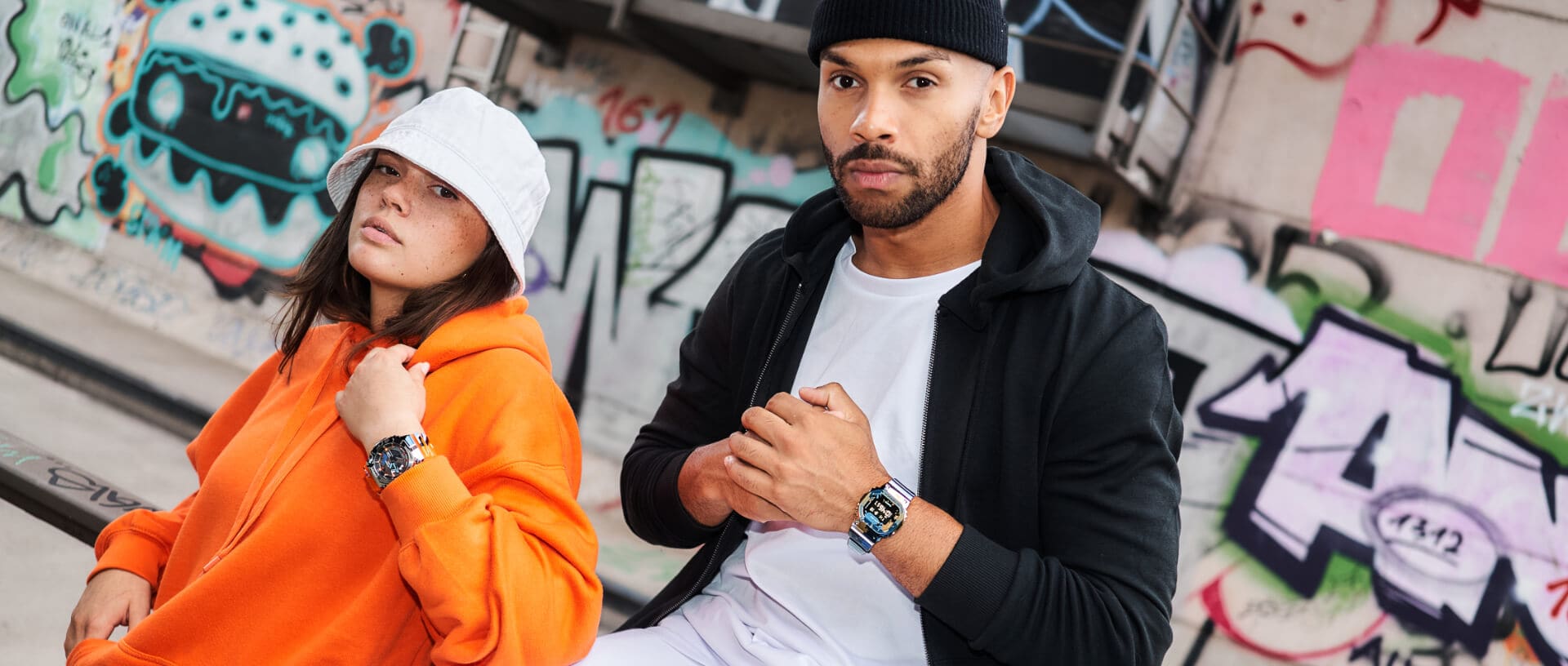 Due modelli indossano abiti casual e sono seduti davanti a un muro ricoperto di graffiti, con al polso gli orologi G-SHOCK GA-110SS e DW-5000SS.