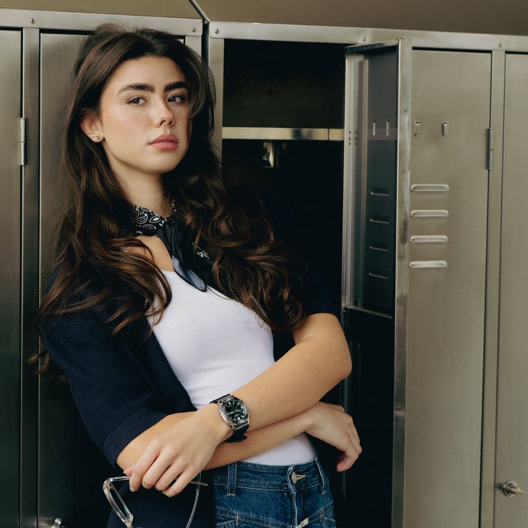 Una ragazza appoggiata a un armadietto indossa il modello GBM-2100A-1A3 con quadrante verde e lunetta in metallo.