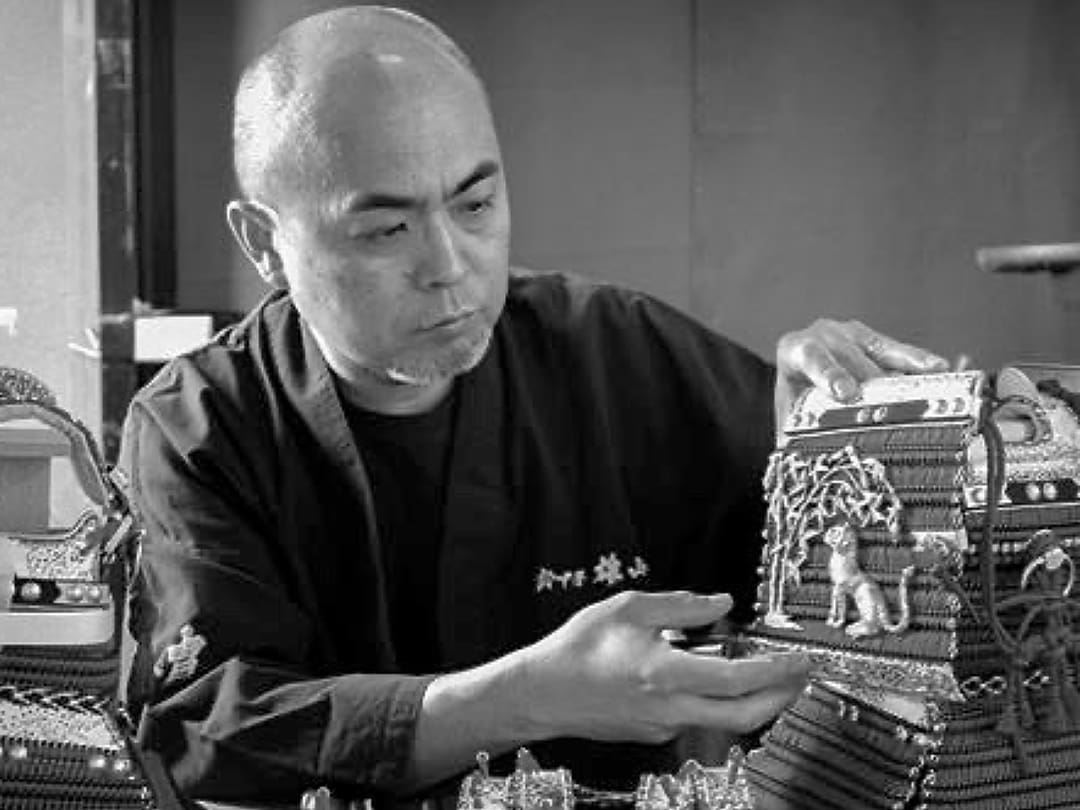 Il fabbricante di elmi Suzukine Yuzan in abito nero esamina un'armatura con decorazioni