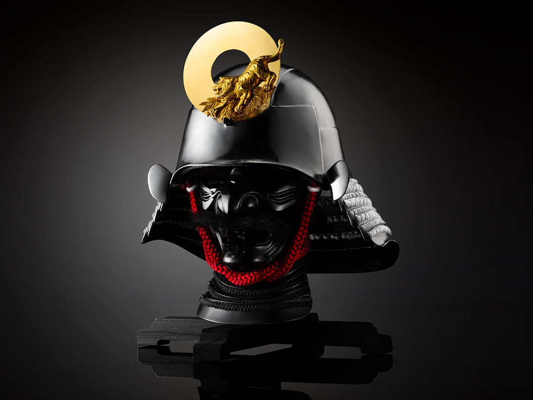 Un casco nero con decorazioni dorate a forma di tigre e un cordone rosso su un busto nero.