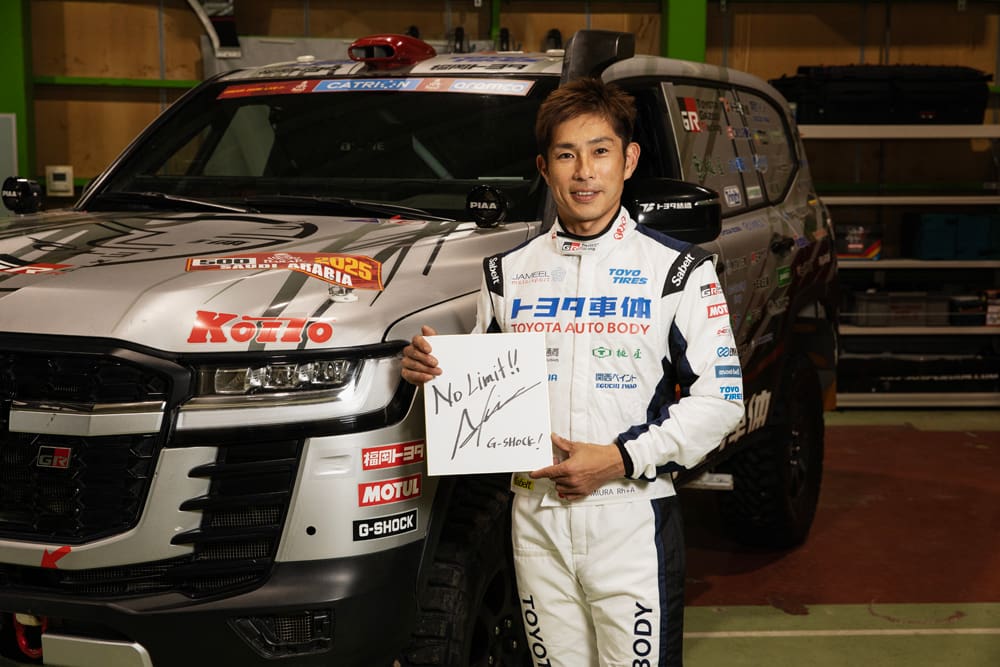 サイン色紙を持ちランドクルーザーの前に立つ三浦昂ドライバー