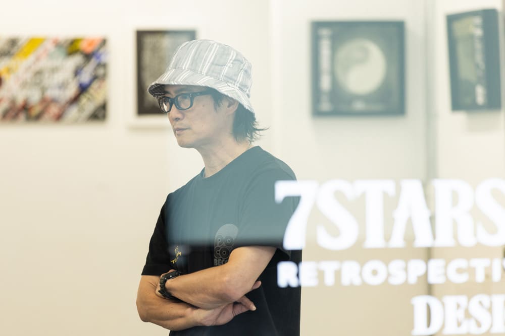 7Stars Designのロゴの後ろに立つ堀内俊哉