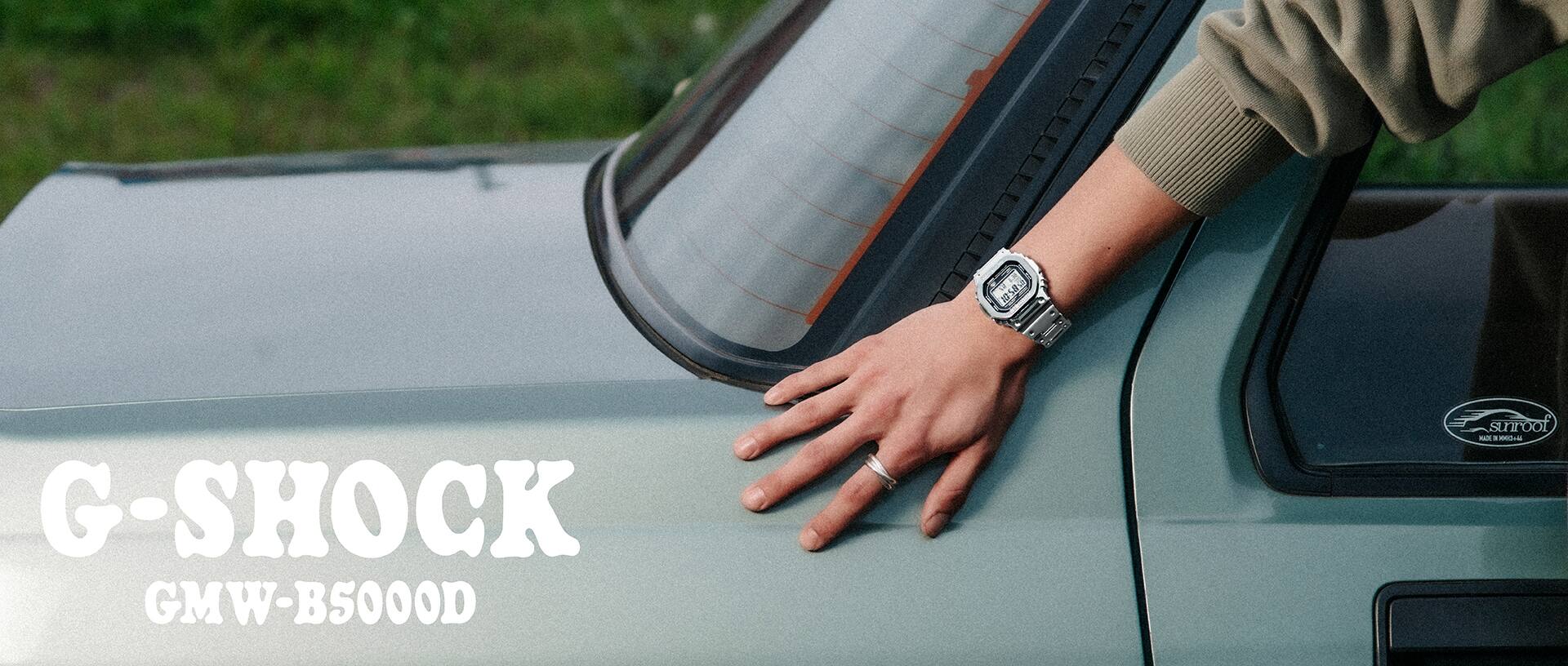 បុរស​ម្នាក់​ពាក់​នាឡិកា G-SHOCK GMW-B5000D កំពុងផ្អែក​លើរថយន្ត។