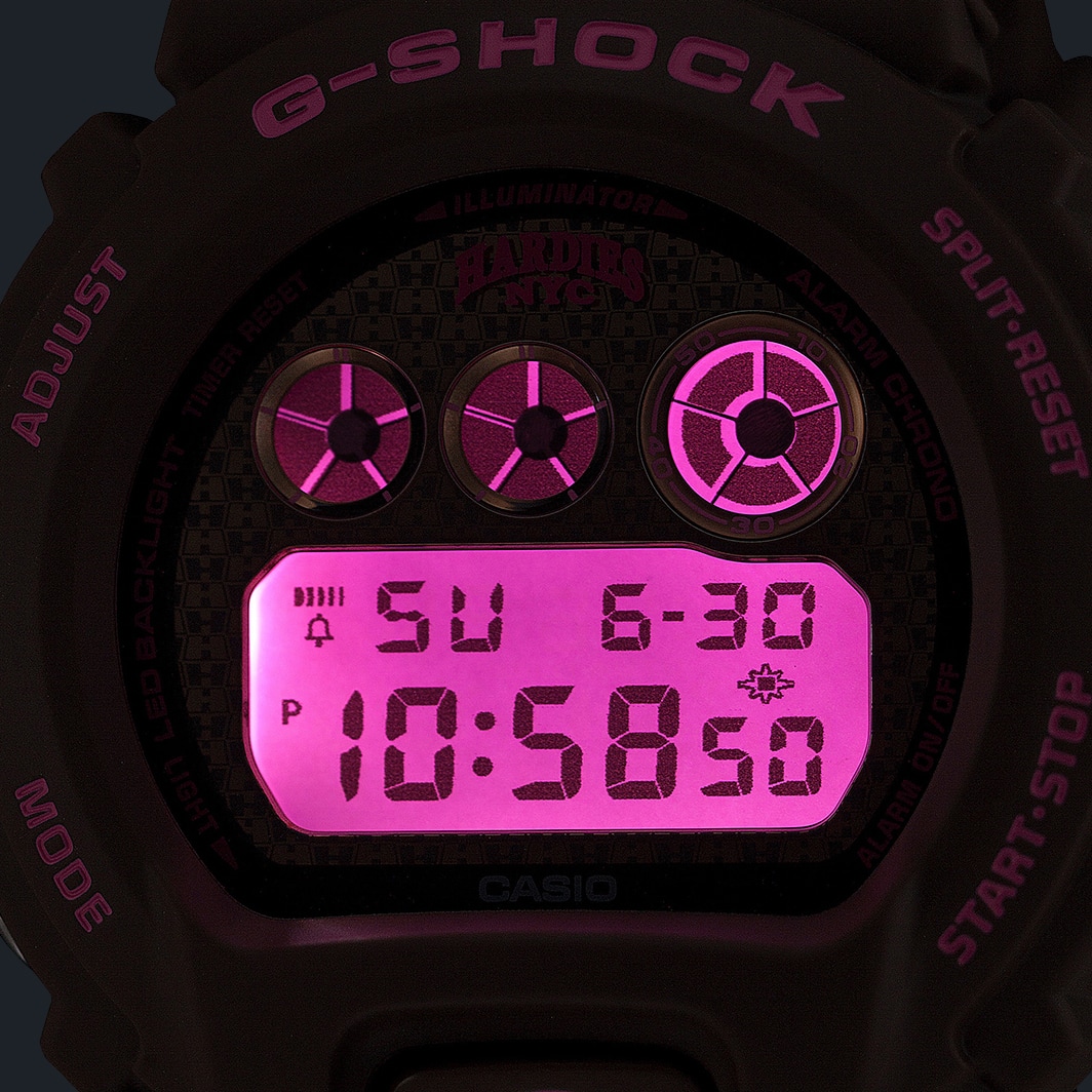 어두운 환경에서 핑크 디지털 디스플레이에 불빛이 들어온 G-SHOCK DW-6900HH-5를 촬영한 사진.