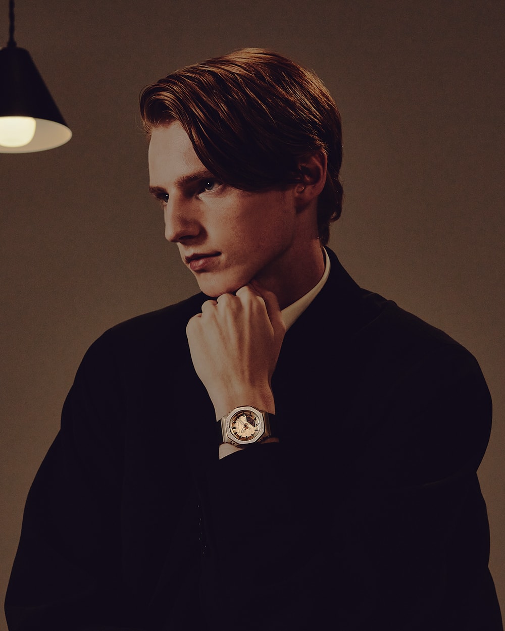 G-SHOCK GM-S2110BP en la muñeca de un hombre en un traje con una mano apoyada en su mentón.