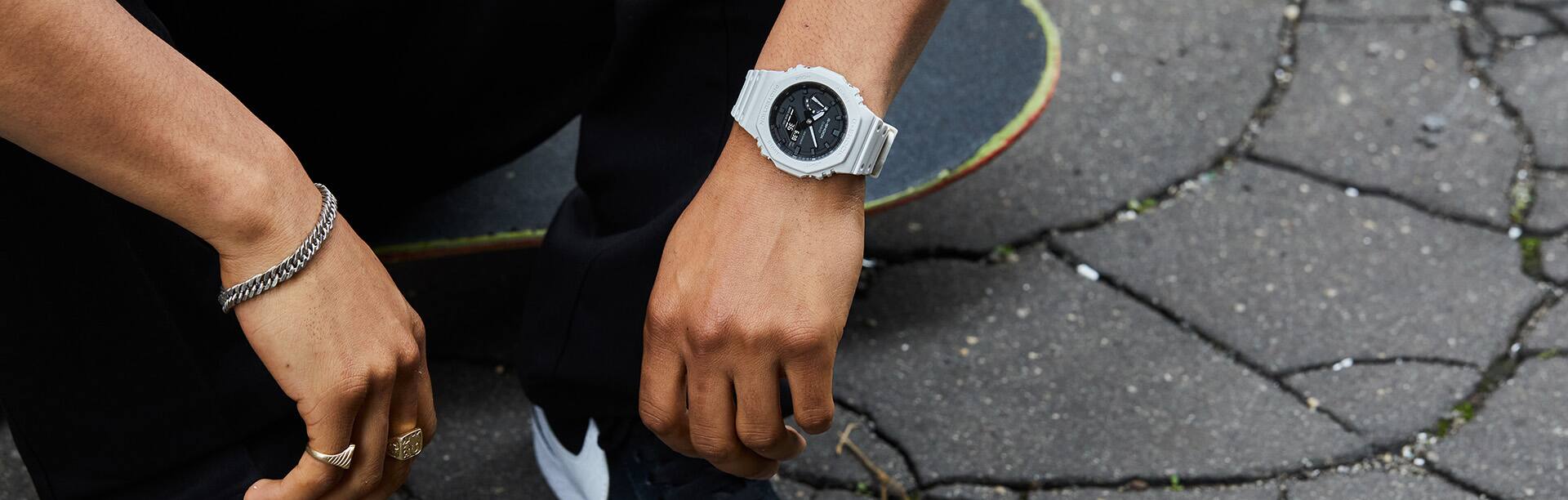 Skateboarder, male, sitting on his skateboard in an urban setting with a GA2100-7A watch on his wrist. Skateboarder, male, sitting on his skateboard in an urban setting with a GA2100-7A watch on his wrist.