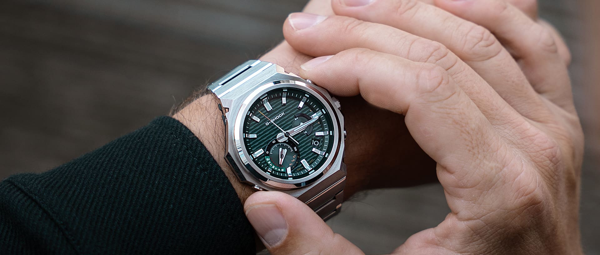 Close-up van de pols van een man die het zilveren GST-B1000-polshorloge  met groene, analoge wijzerplaat draagt.