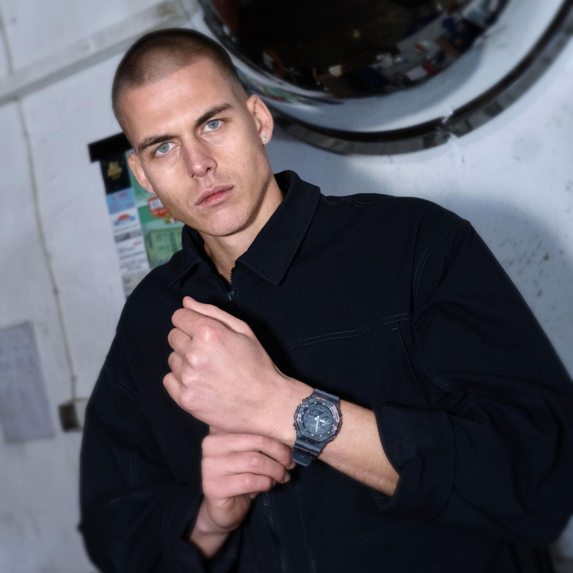 Een man in donkere kleding staat in een werkplaats en draagt een G-SHOCK GA-2100CM-8AER om zijn pols.