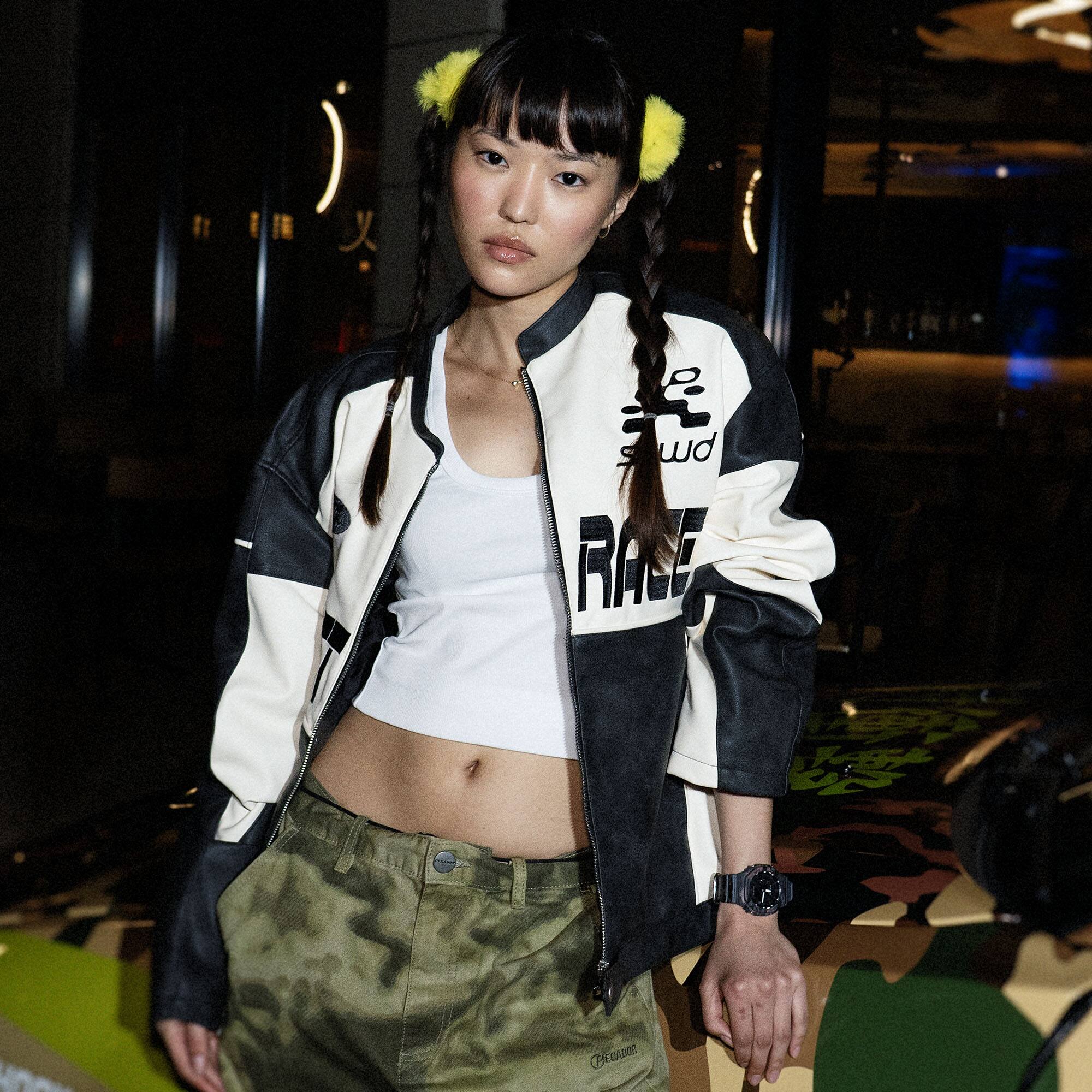 Een vrouw met twee vlechten en een nonchalante outfit staat voor de Nissan met camouflageprint. Om haar pols is de G-SHOCK GA-2100CM-8A te zien met een analoge wijzerplaat en een band met patroon.