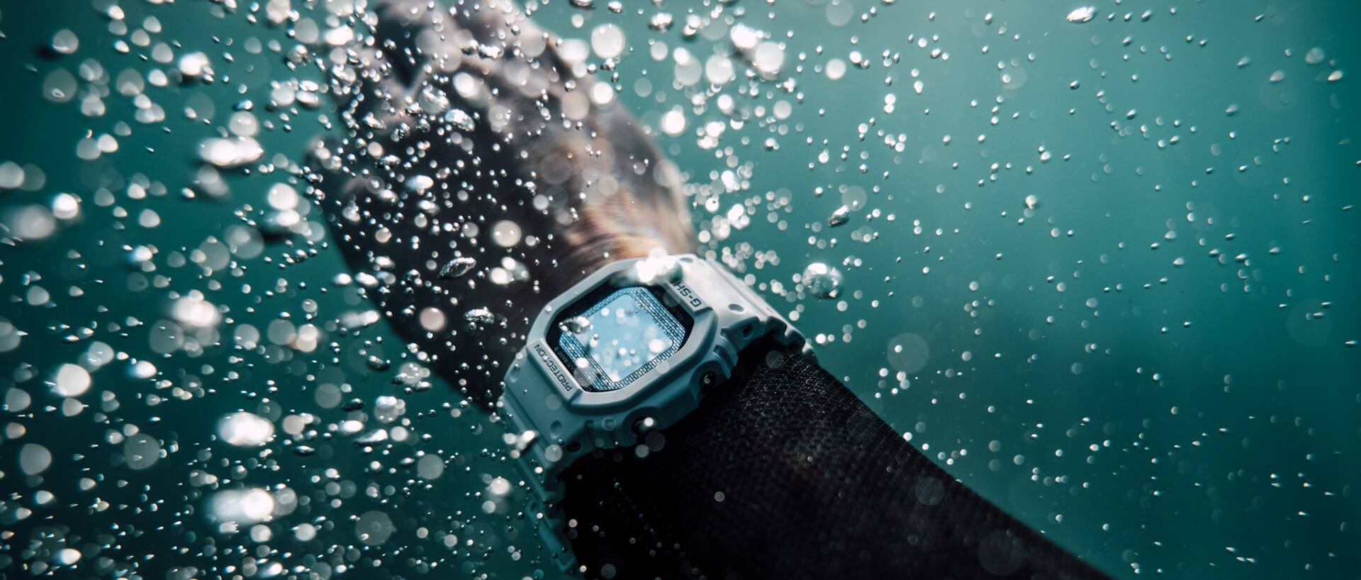 Eén arm draagt de witte GW-5000HS-7ER onder water met opstijgende luchtbellen.