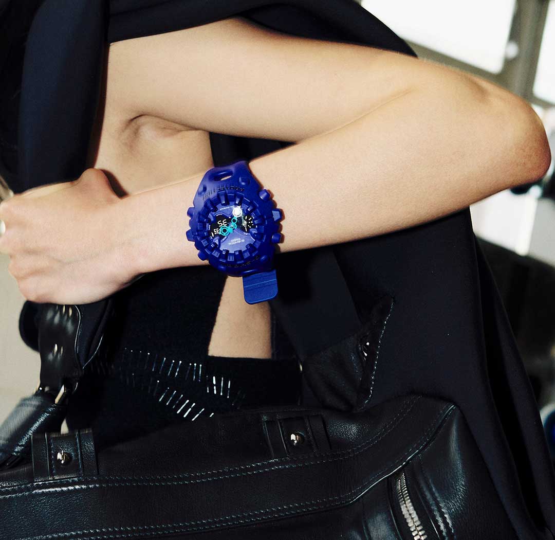 Halflange opname van een vrouw in zwarte kleding met het paarse GA-V01 polshorloge van G-SHOCK om haar pols