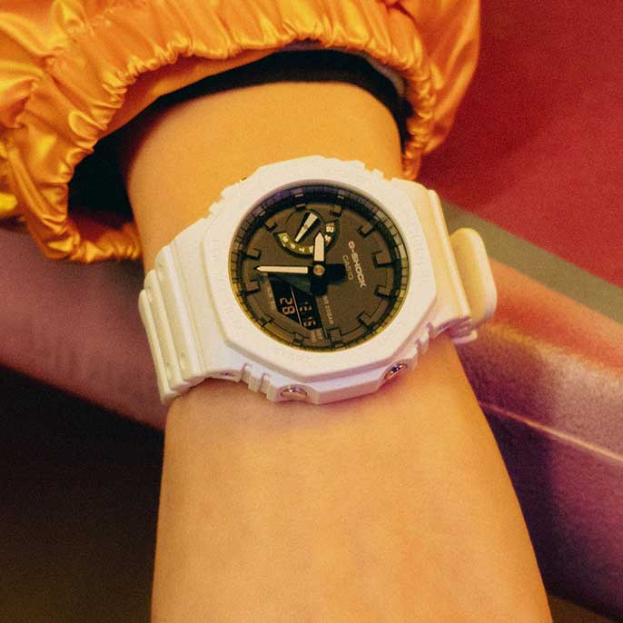 O relógio de pulso G-SHOCK GA-2100-7A branco com mostrador analógico preto e pequeno mostrador digital da data no pulso de uma pessoa