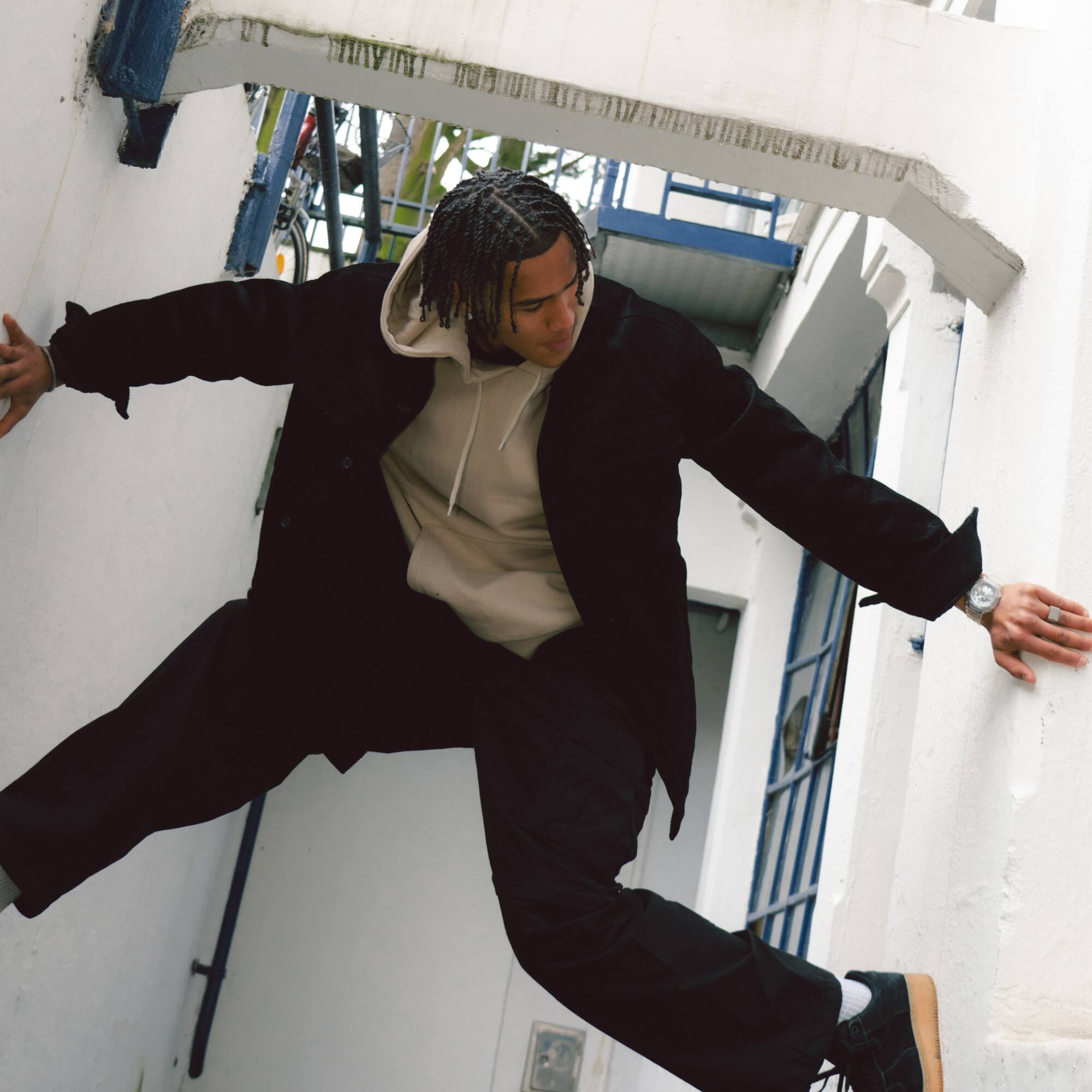 Um homem de roupa preta enfia-se entre duas paredes e olha para o seu pulso esquerdo, no qual tem o GA-2100BM com um mostrador prateado.