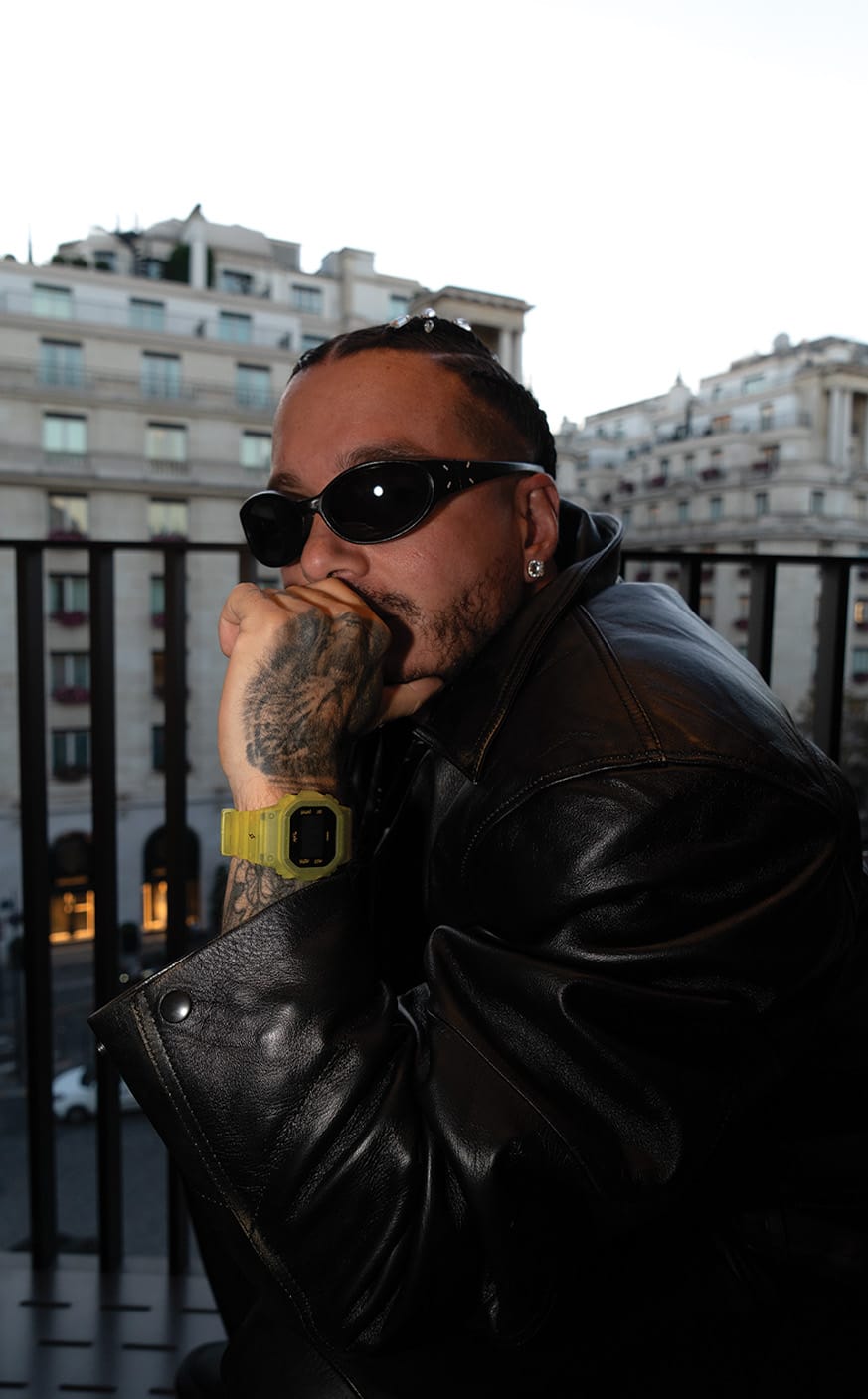 O rapper J-Balvin usa óculos de sol, um casaco de cabedal preto e o relógio amarelo brilhante da colaboração G-SHOCK