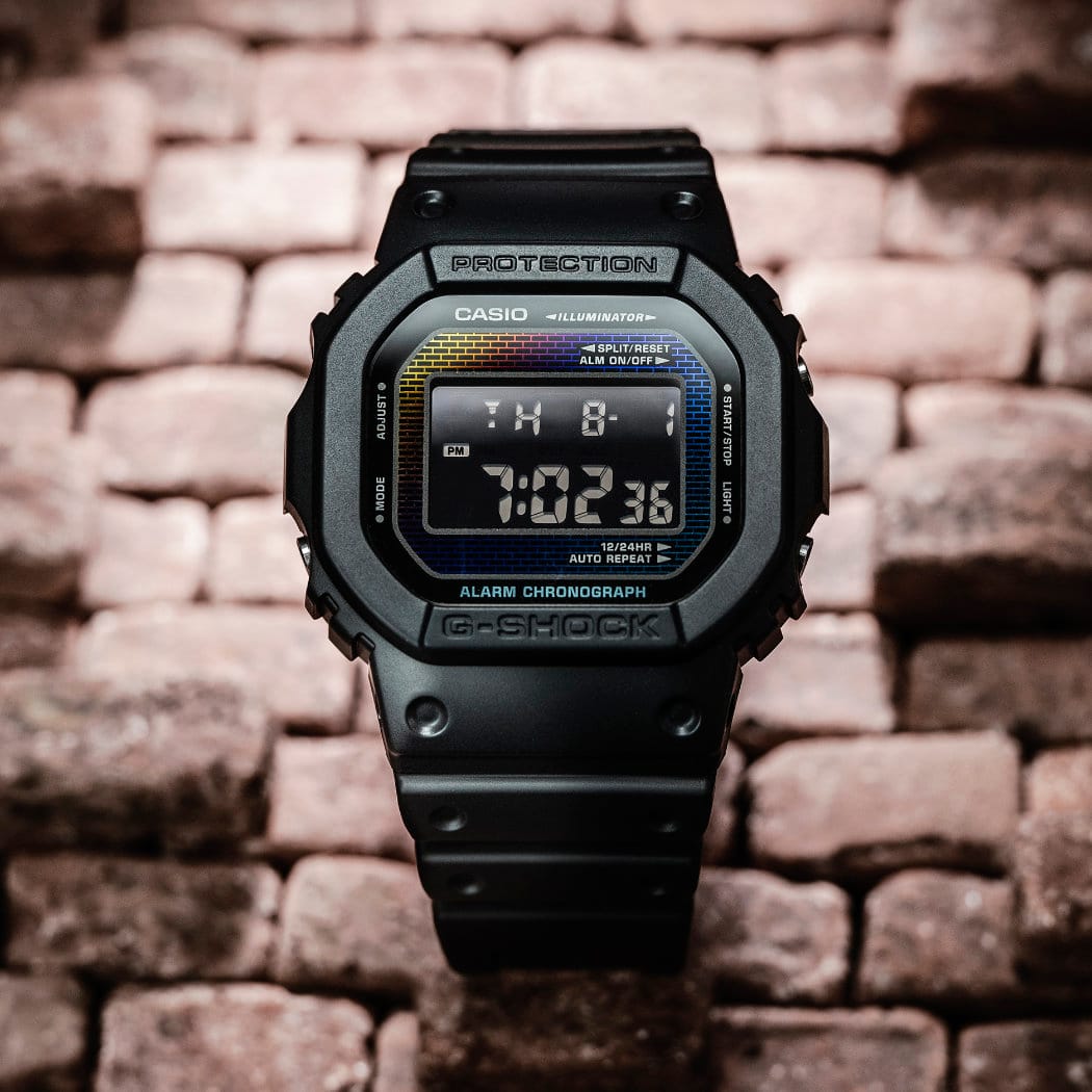 O relógio DW-5600RW-1ER da G-SHOCK com bracelete e caixa pretas em frente a uma parede de tijolo