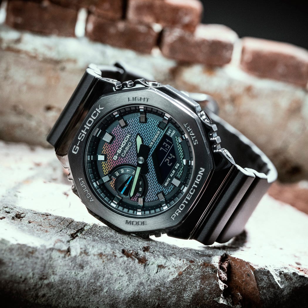 O relógio analógico com bracelete metálica "GM-2100BRW-1AER" da G-SHOCK em cima de uma parede de tijolo