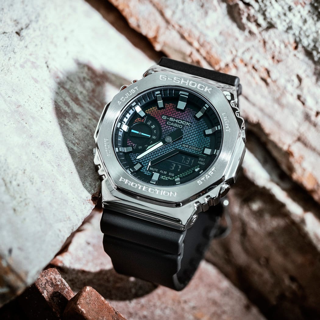 O relógio de pulso "GM-2100RW-1AER" com luneta de metal e bracelete de resina preta colocado em frente a uma parede de tijolo.