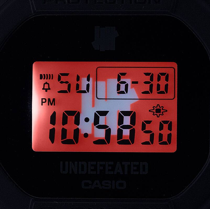 O logótipo UNDEFEATED no mostrador LCD iluminado do DWE-5600UD-1