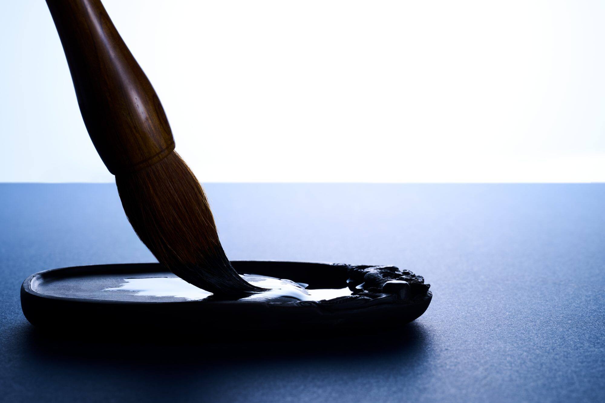 Pode ver-se um pincel castanho-escuro mergulhado em tinta azul-acinzentada escura.