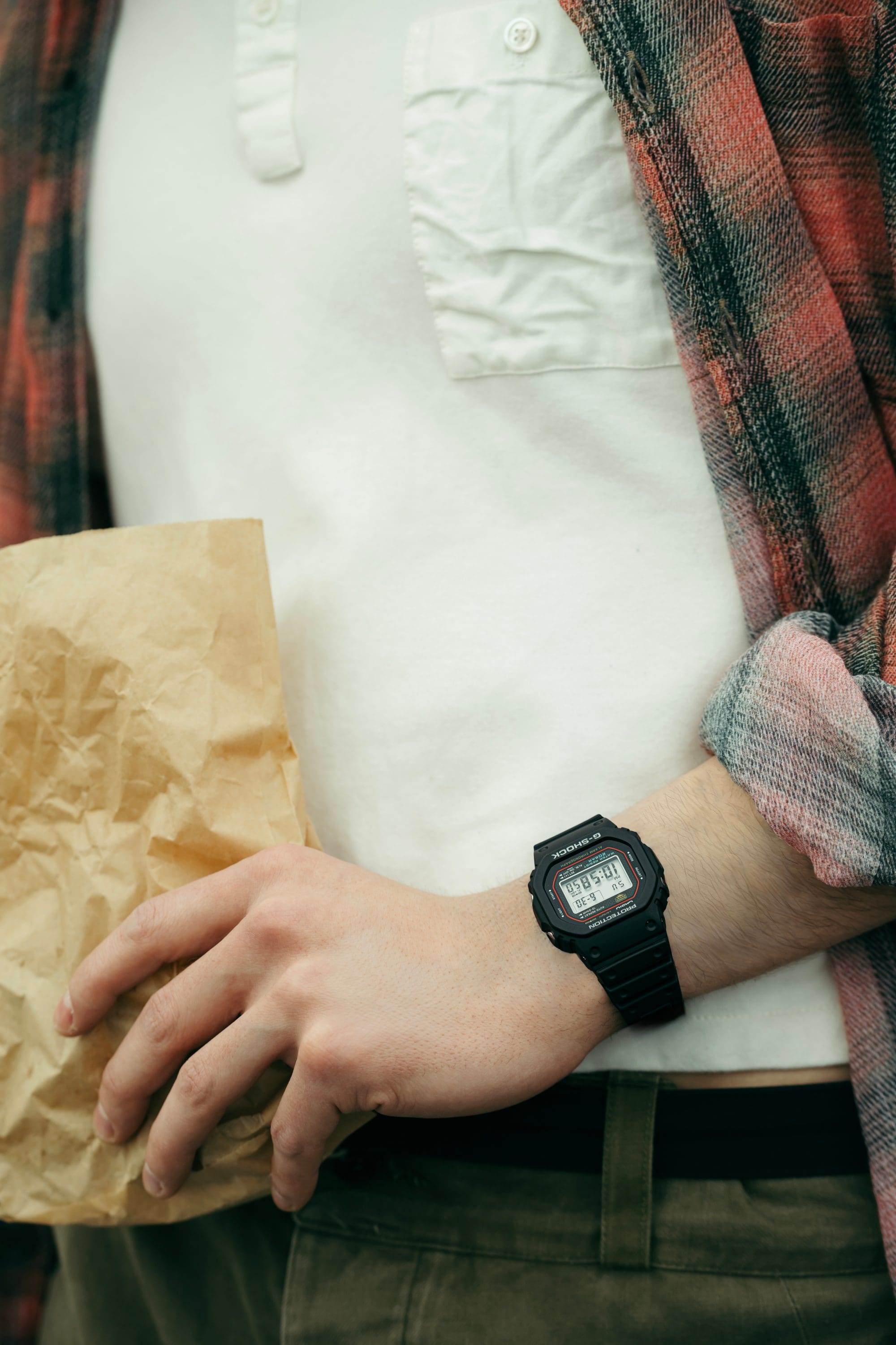 Close-up of wrist wearing G-SHOCK DW-5600R while holding a paper bag.
