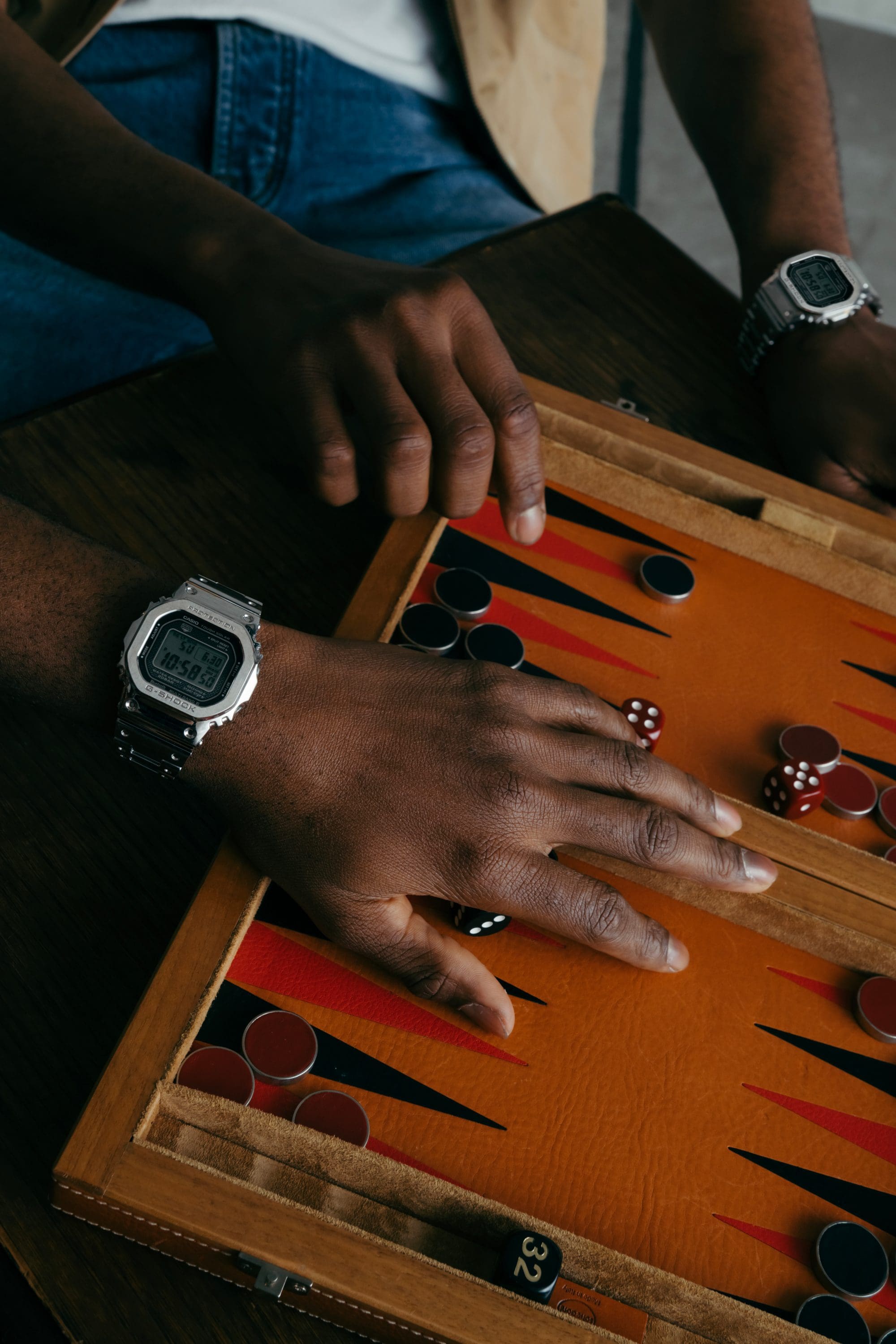 Hands moving game pieces while wearing G-SHOCK GM-5600D on a wooden board.