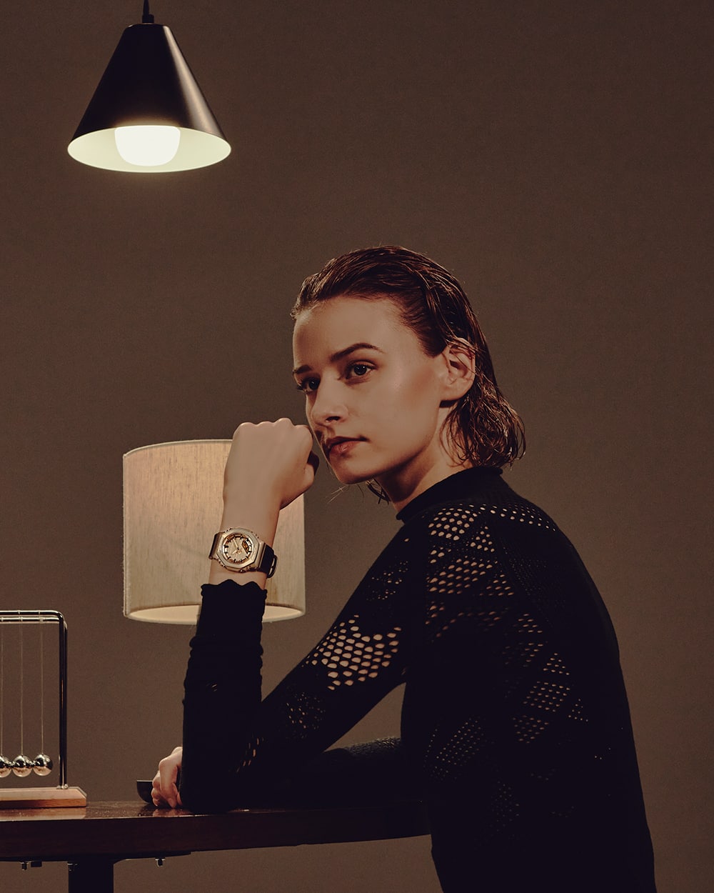 G-SHOCK GM-S2110BP, on the wrist of a woman sitting with one hand resting on her chin.