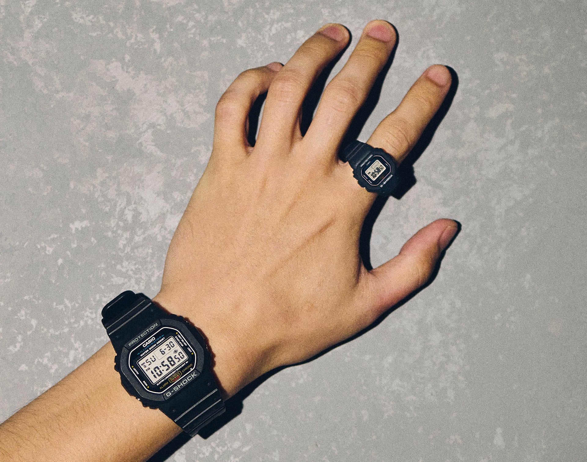 A photo of a man wearing a conventional G-SHOCK watch with a G-SHOCK NANO on his finger