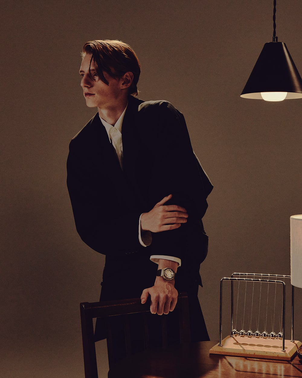 Sol eliyle bir sandalyeyi tutan takım elbise giymiş bir erkeğin bileğindeki G-SHOCK GM-S2110BP.