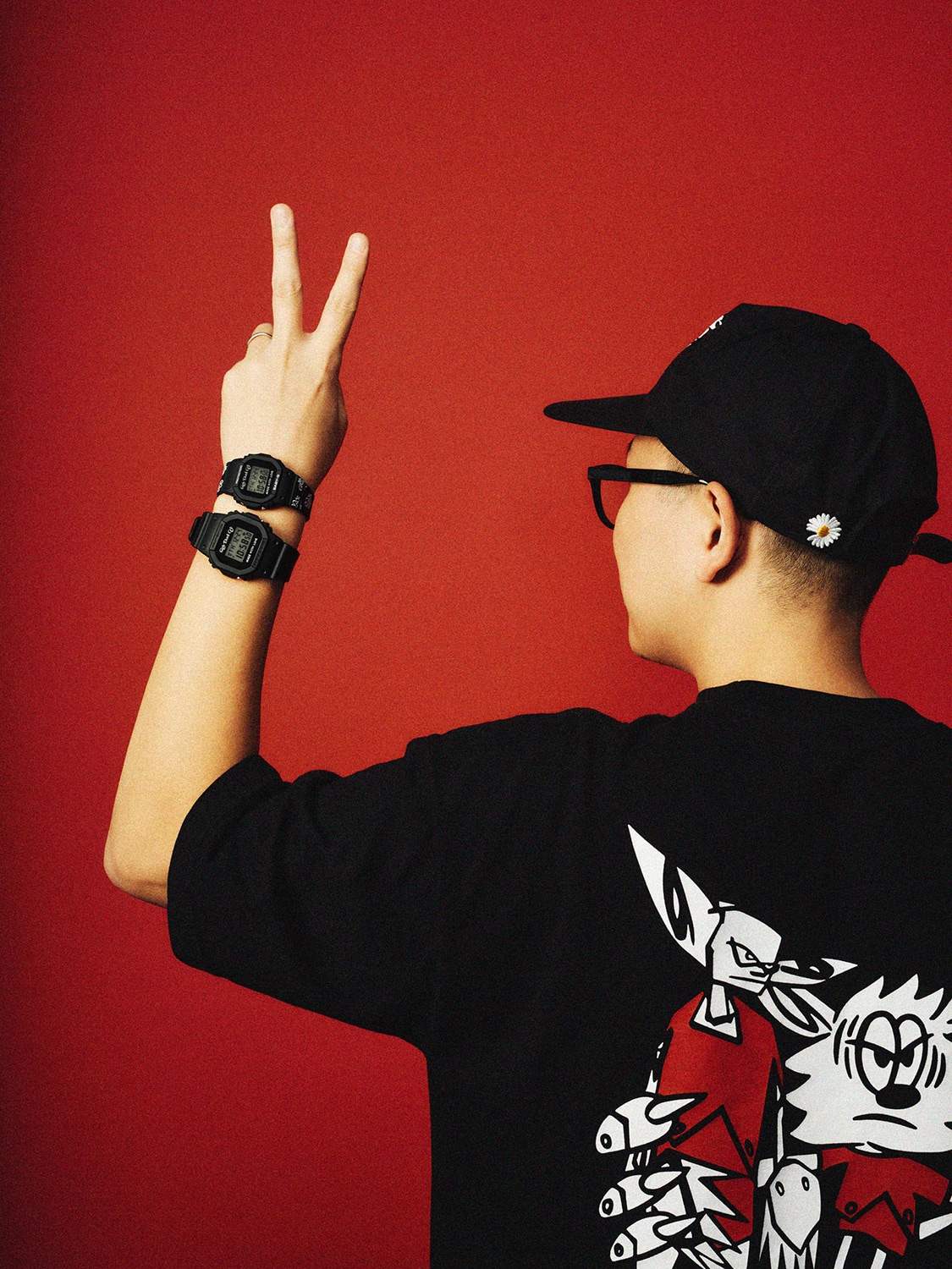 A photo of VERDY wearing a black T-shirt, cap and G-SHOCK watch against a red backdrop.