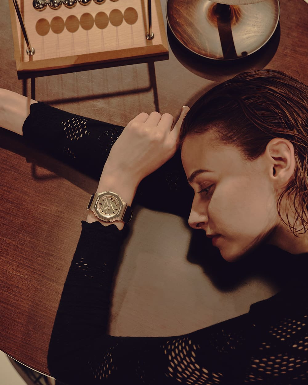 G-SHOCK GM-S2110BP，佩戴在倚靠桌面的女子手腕上。