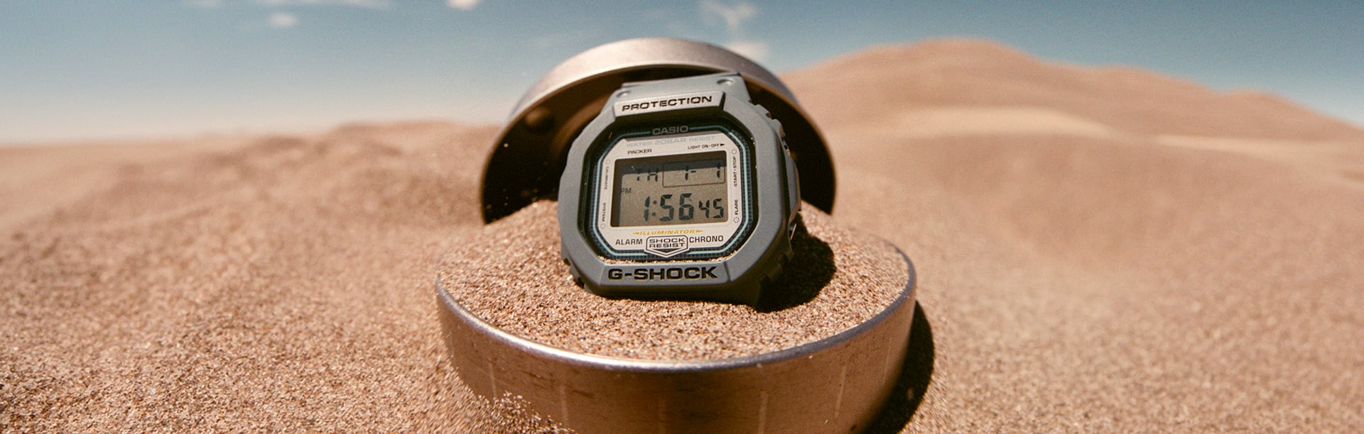 G-SHOCK X PACKER DW5600PCK23-2B gray digital watch in a sand dune