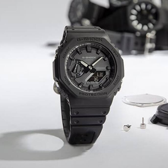 Black GA2100 Series analog digital watch with other watches and parts in the background