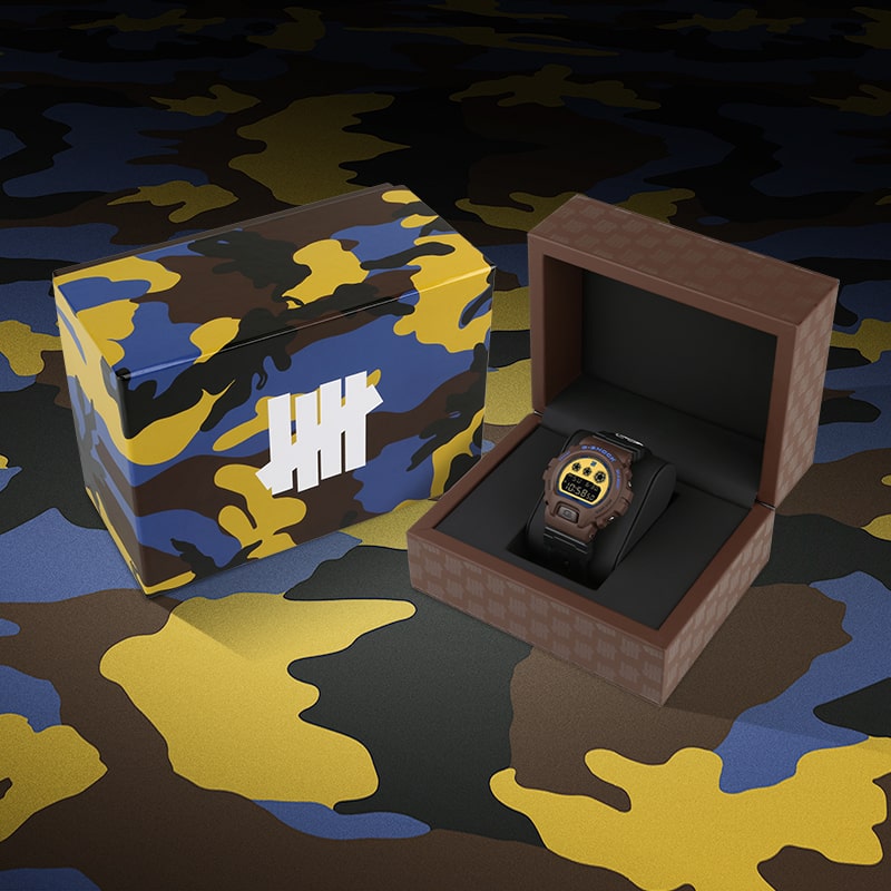 G-SHOCK x UNDEFEATED DW6900UDCR235 40th anniversary watch in its special packaging with a brown, yellow and blue camoflauge that matches the outer box design