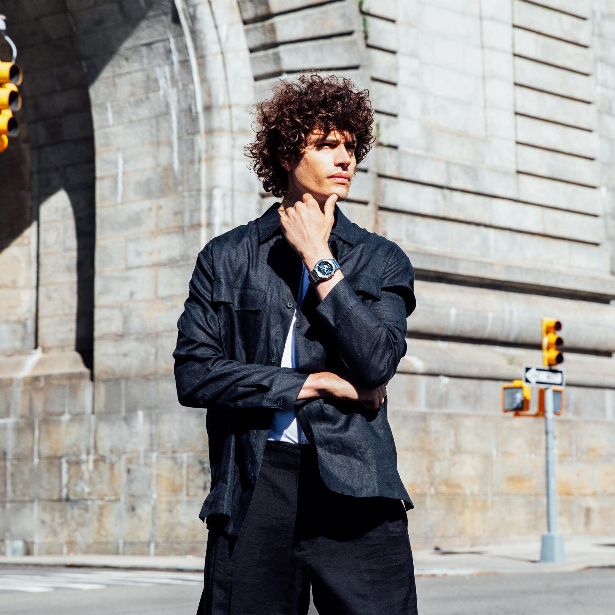 Medium shot of a man in a black jacket standing near a building wearing a G-SHOCK GM2110D- 2B watch denoting style