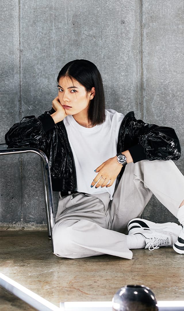 Woman sitting on the floor leaning on a chair wearing a gms110 metal covered analog digital watch