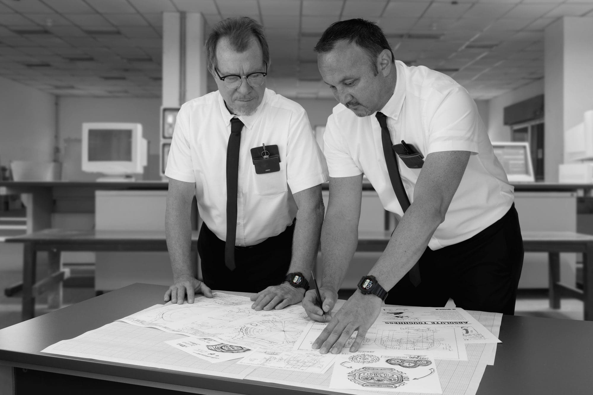 A black-and-white image of two men wearing the G-SHOCK GW6900NASA24-1 NASA Watch perusing design schematics A black-and-white image of two men wearing the G-SHOCK GW6900NASA24-1 NASA Watch perusing design schematics