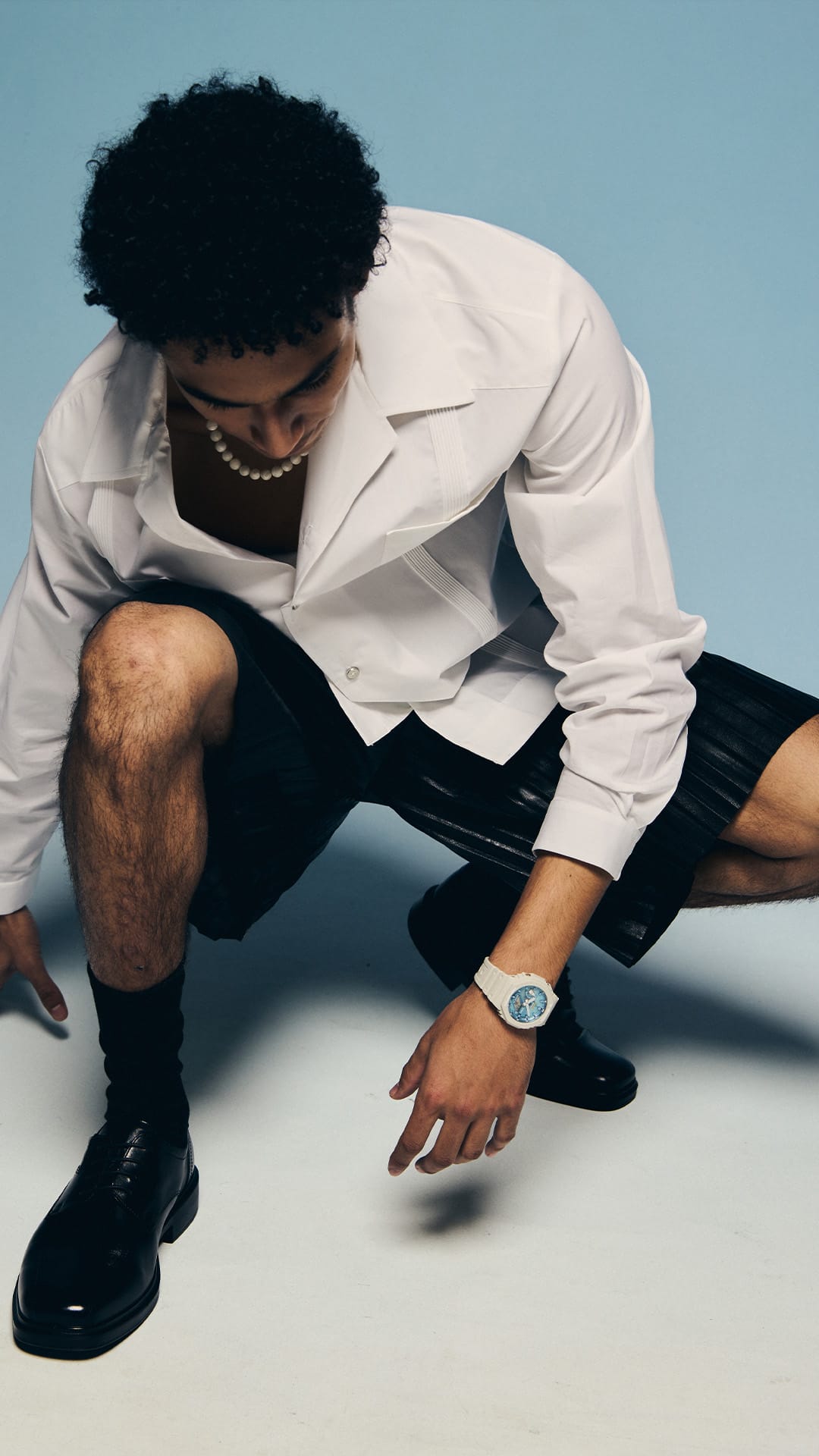 Man crouching in a white shirt wearing the G-SHOCK GA2100AS-5A blue-dial watch denoting style