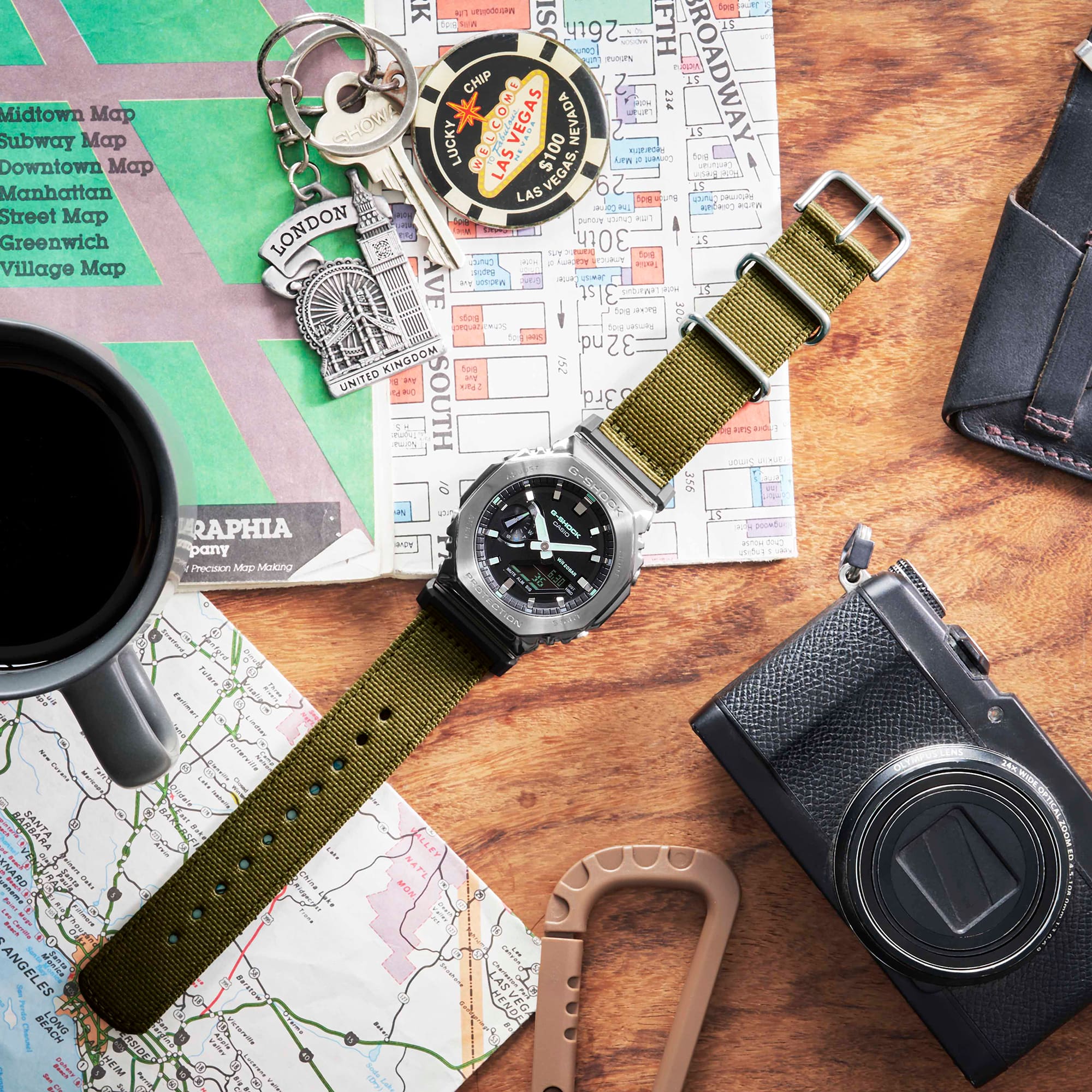 G-SHOCK GM2100CB-3A Metal covered analog digital utility watch with cloth band on a desk with map and other adventuring materials G-SHOCK GM2100CB-3A Metal covered analog digital utility watch with cloth band on a desk with map and other adventuring materials