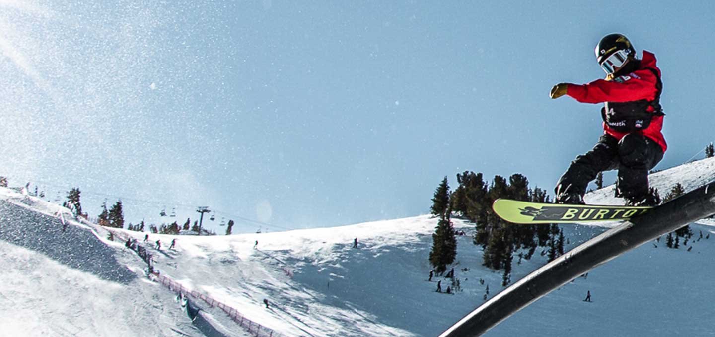 Snowboarder doing a trick on a rail in fronot of ski slope