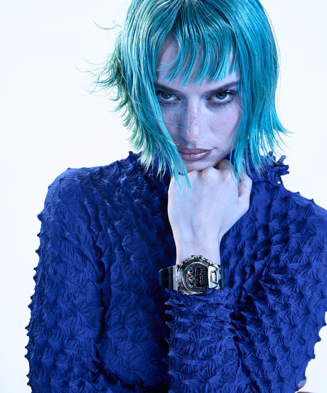 Person with bright blue hair wearing a textured blue top and a G-SHOCK watch.
