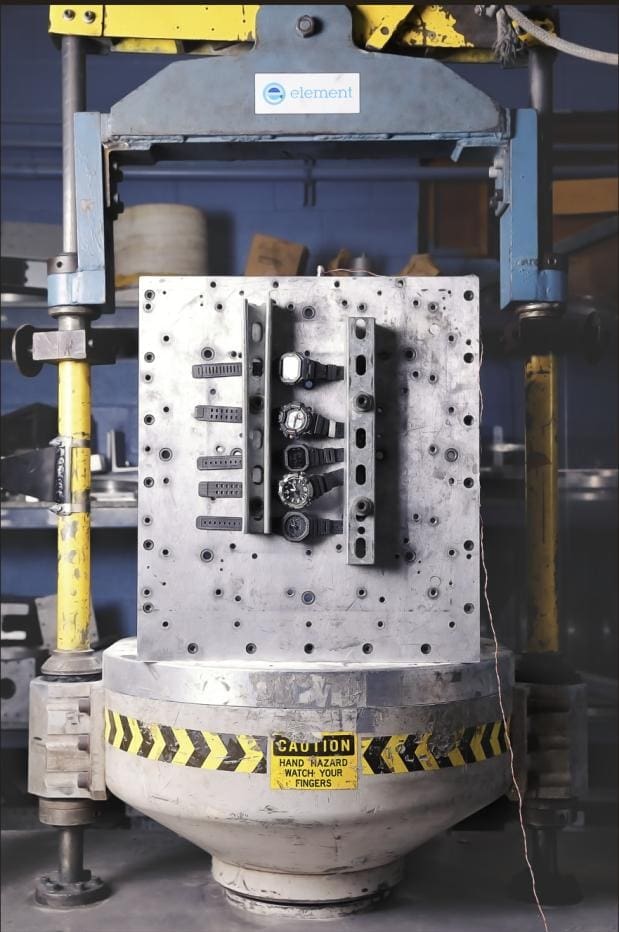 Five G-SHOCK mil-spec watches secured to a mechanical shock test fixture inside an industrial test machine.