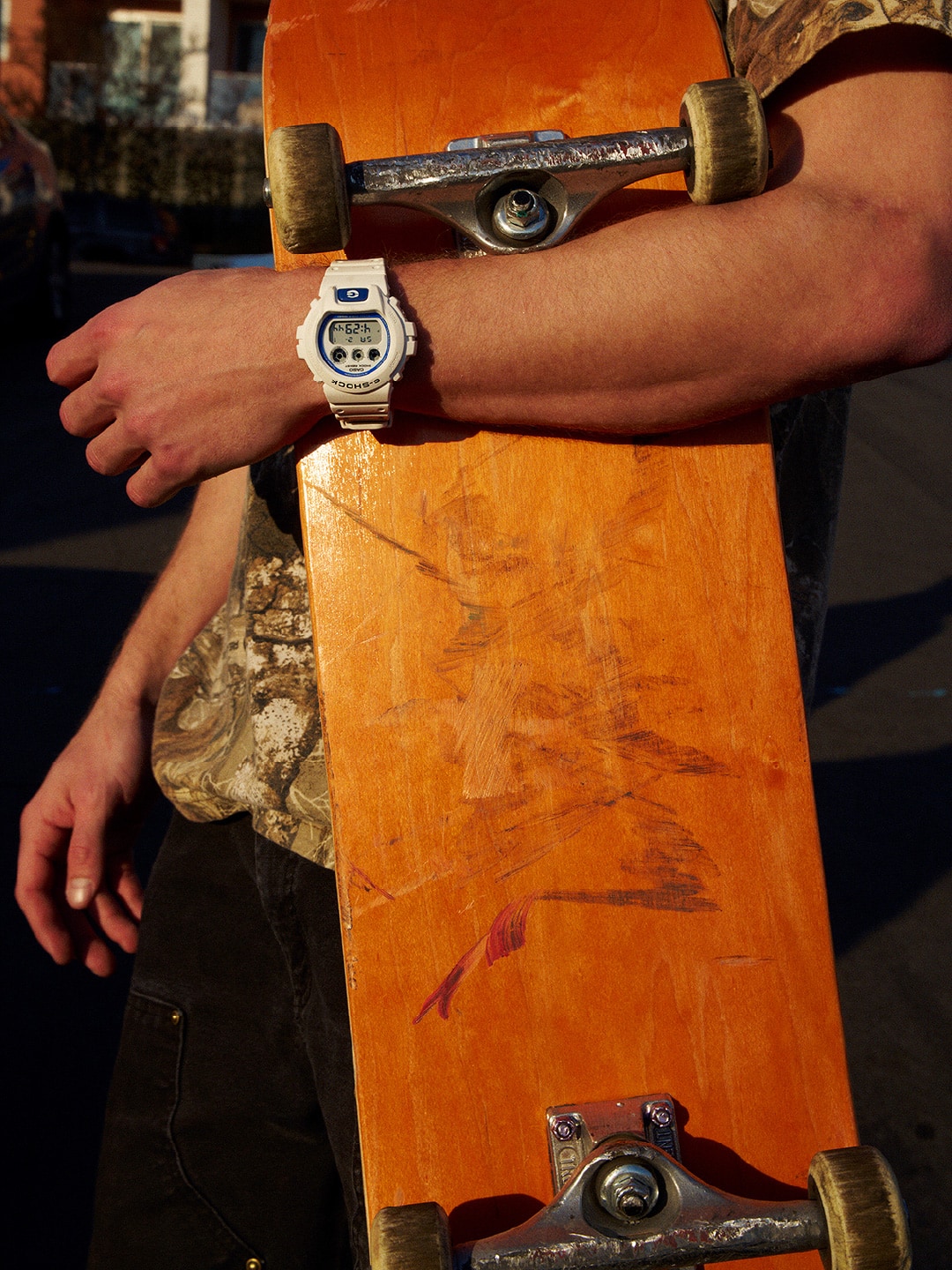 شخص يرتدي ساعة G-SHOCK باللون الأبيض ويحمل لوح تزلج.