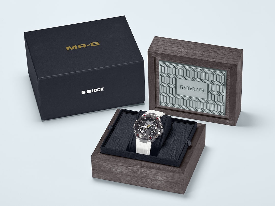 Die dunkle Umverpackung mit goldener MR-G-Prägung neben der hochwertigen Geschenkbox aus Kiri-Holz mit dem MRG-B2000SG-1A Chronographen