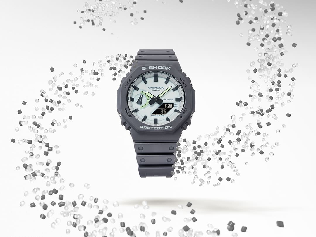 GA-2100HD-8A Die GA-2100HD-8A Hybriduhr umgeben von einem Wirbel aus durchsichtigen und grauen Resin-Granulat