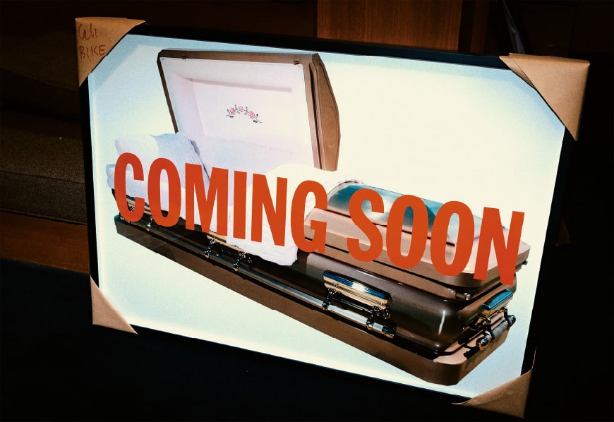 Ein gerahmtes Bild eines Sarges mit der Aufschrift „coming soon“ in großen roten Buchstaben